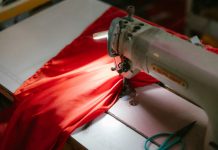 BREAKING: New York Sewing Center to Open Jersey City Location Close-up of an industrial sewing machine stitching bright red fabric, highlighted under a spotlight.
