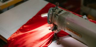 Close-up of an industrial sewing machine stitching bright red fabric, highlighted under a spotlight.