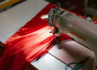 Close-up of an industrial sewing machine stitching bright red fabric, highlighted under a spotlight.