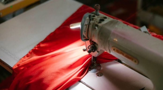 Close-up of an industrial sewing machine stitching bright red fabric, highlighted under a spotlight.