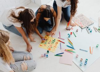 Group of women designing artistic placards with colorful materials.