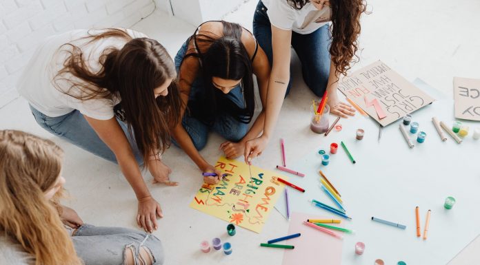 Group of women designing artistic placards with colorful materials.