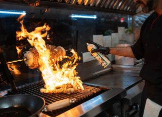 Chef uses a culinary torch to ignite a flaming grill indoors, showcasing dynamic cooking.