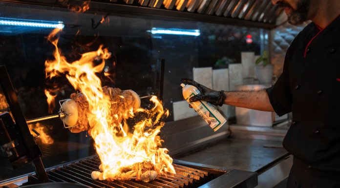 Chef uses a culinary torch to ignite a flaming grill indoors, showcasing dynamic cooking.