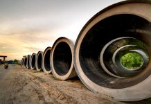 Columbus Drive Redo Delayed as Water Lines Take Priority Massive concrete pipes aligned at a construction site during sunset, showcasing an industrial landscape.