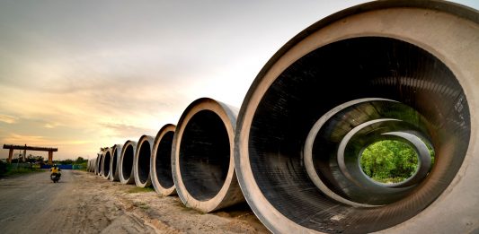 Massive concrete pipes aligned at a construction site during sunset, showcasing an industrial landscape.