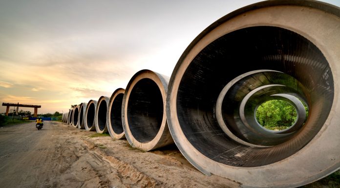 Columbus Drive Redo Delayed as Water Lines Take Priority Massive concrete pipes aligned at a construction site during sunset, showcasing an industrial landscape.