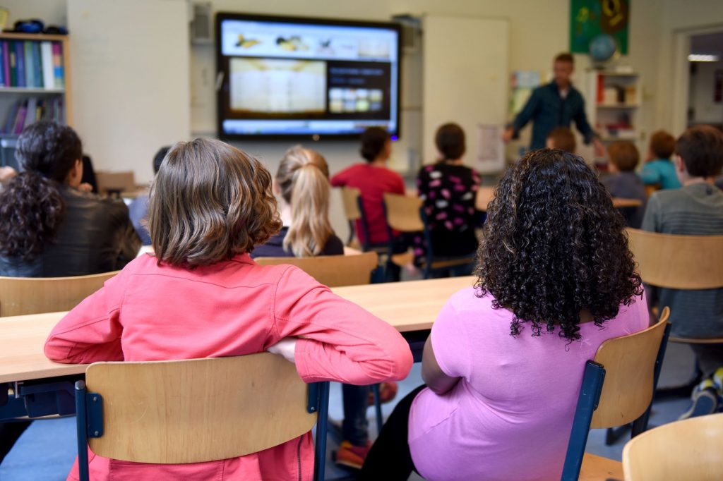 Students attentively watching a lesson on a smart board in a colorful Dutch classroom.