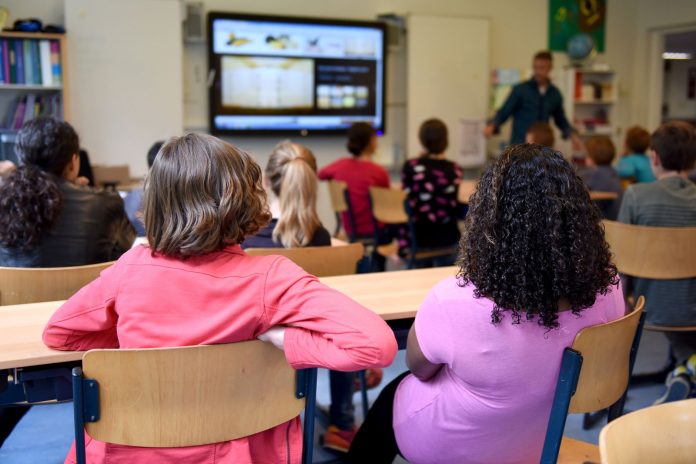 Students attentively watching a lesson on a smart board in a colorful Dutch classroom.