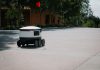 A sleek autonomous food delivery robot navigates a sunny urban landscape, showcasing modern innovation.