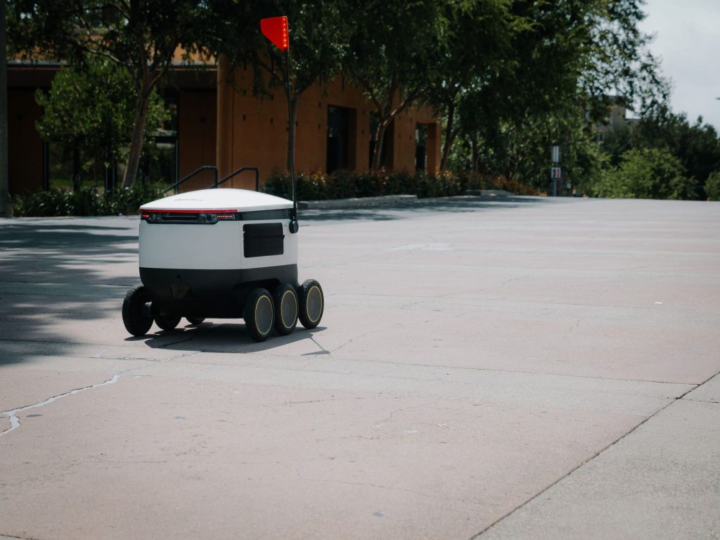 A sleek autonomous food delivery robot navigates a sunny urban landscape, showcasing modern innovation.