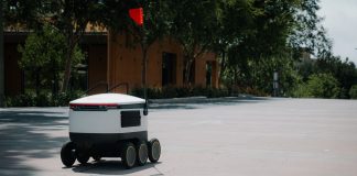 A sleek autonomous food delivery robot navigates a sunny urban landscape, showcasing modern innovation.