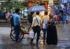 A vibrant street view showcasing people conversing under an umbrella on a rainy day.
