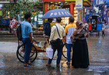 A vibrant street view showcasing people conversing under an umbrella on a rainy day.