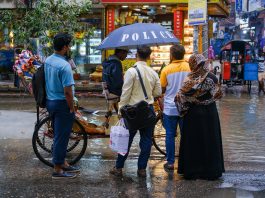 A vibrant street view showcasing people conversing under an umbrella on a rainy day.