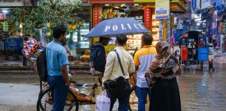 A vibrant street view showcasing people conversing under an umbrella on a rainy day.