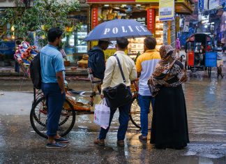 A vibrant street view showcasing people conversing under an umbrella on a rainy day.