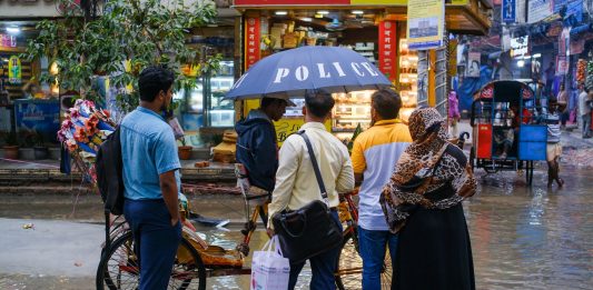 A vibrant street view showcasing people conversing under an umbrella on a rainy day.