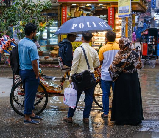 A vibrant street view showcasing people conversing under an umbrella on a rainy day.