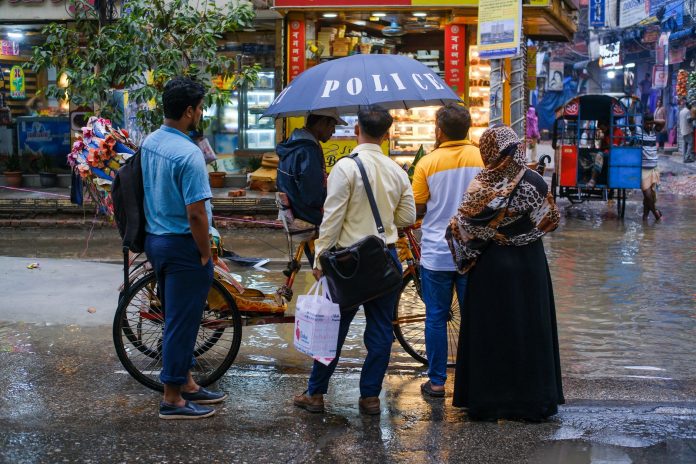 A vibrant street view showcasing people conversing under an umbrella on a rainy day.