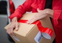 A courier in red uniform sealing a cardboard package with red tape for delivery.
