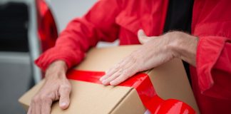 A courier in red uniform sealing a cardboard package with red tape for delivery.