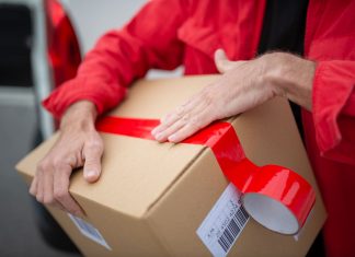 A courier in red uniform sealing a cardboard package with red tape for delivery.