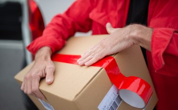 Former Jersey City Postal Worker Admits Burglarizing Post Offices A courier in red uniform sealing a cardboard package with red tape for delivery.
