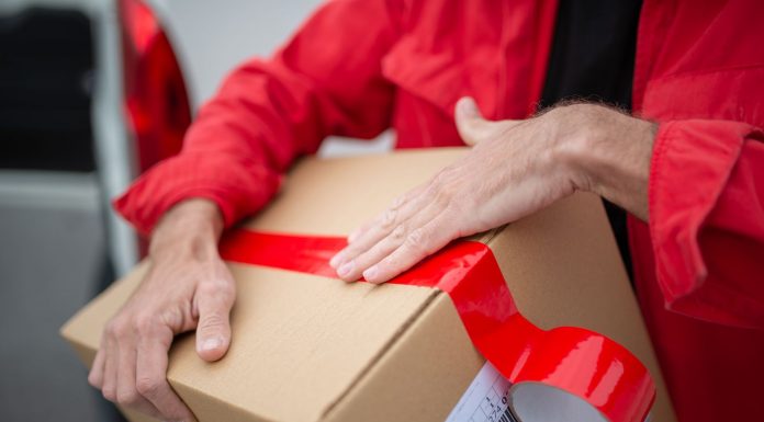 A courier in red uniform sealing a cardboard package with red tape for delivery.