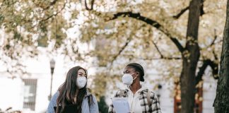 Low angle of diverse classmates in masks with folders talking about university issues while walking in park together
