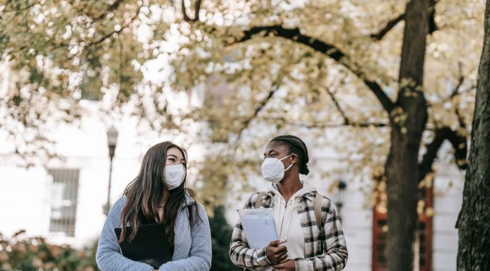 HCCC Wins National Award for Mental Health Work Low angle of diverse classmates in masks with folders talking about university issues while walking in park together