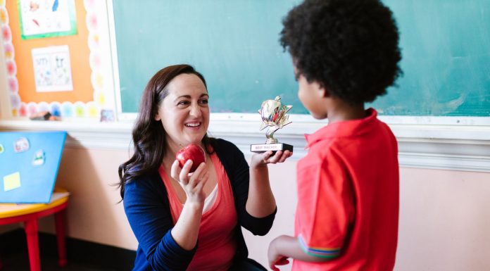 A teacher holding an apple and a student holding a trophy in a classroom setting.