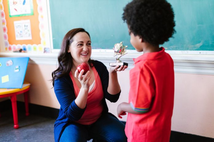 hcst-teacher-wins-hudson-county-honor-for-second-s A teacher holding an apple and a student holding a trophy in a classroom setting.