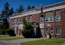 A classic brick schoolhouse in Redfield, NY with a U.S. Post Office, capturing a sunny day.