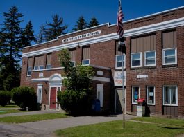 A classic brick schoolhouse in Redfield, NY with a U.S. Post Office, capturing a sunny day.