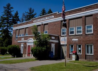 A classic brick schoolhouse in Redfield, NY with a U.S. Post Office, capturing a sunny day.