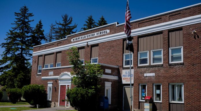 A classic brick schoolhouse in Redfield, NY with a U.S. Post Office, capturing a sunny day.