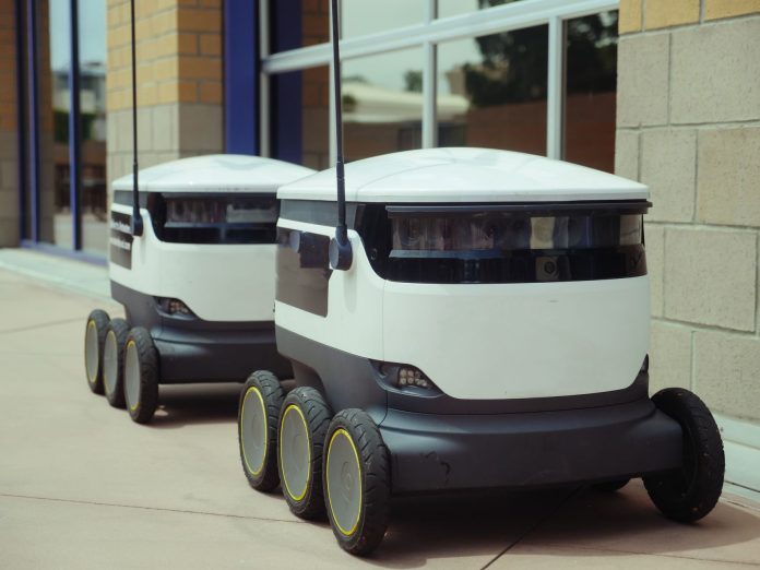 hoboken-approves-delivery-robot-pilot-program Two autonomous delivery robots positioned outside a modern building, showcasing innovation in robotics and mobility.