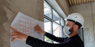 Architect wearing hard hat and mask reviews floor plans on site for new construction project.