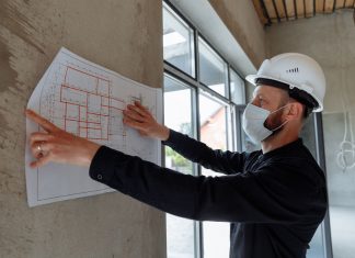 Architect wearing hard hat and mask reviews floor plans on site for new construction project.