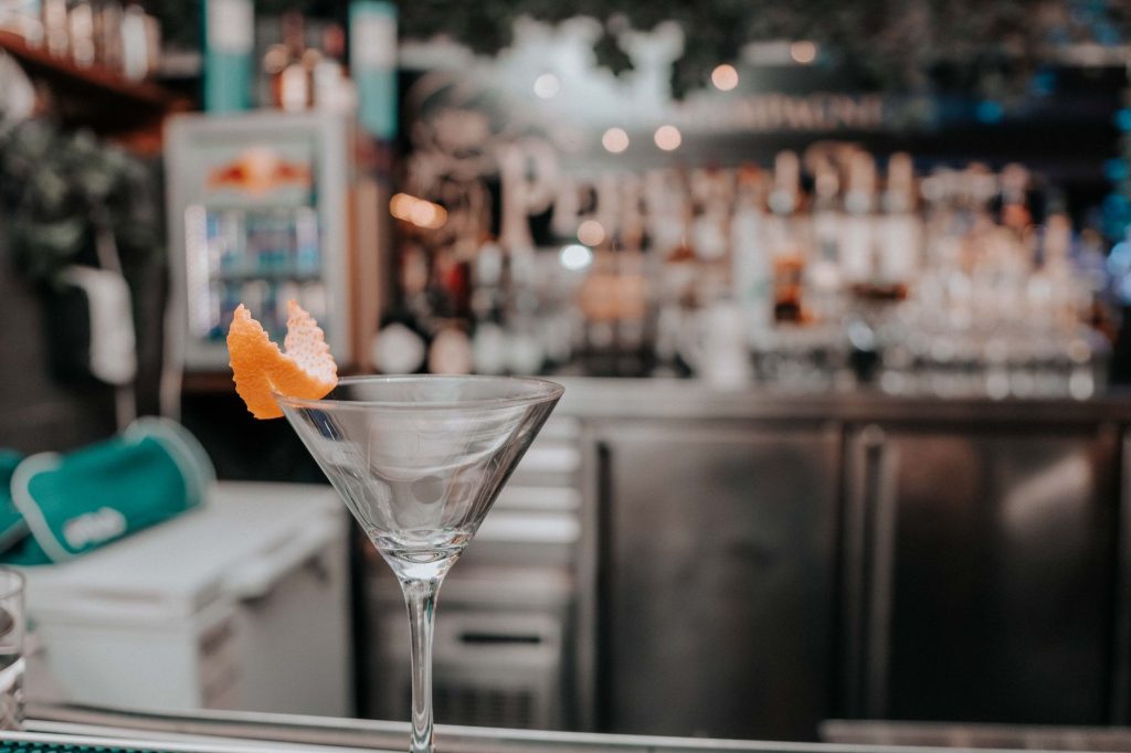 Martini glass with orange peel on bar counter in chic cocktail lounge.