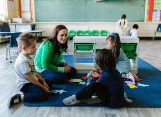 Teacher and children engaged in educational activities on a classroom floor.
