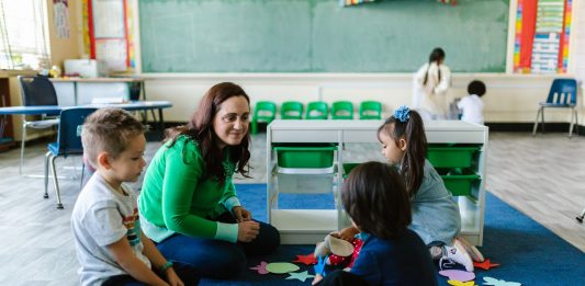 Teacher and children engaged in educational activities on a classroom floor.