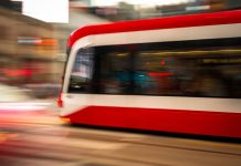 Blurred motion photo of a red tram speeding through city streets, capturing urban energy.