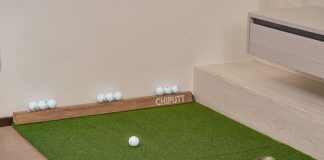 Indoor putting green with golf balls and equipment for golf practice at home.