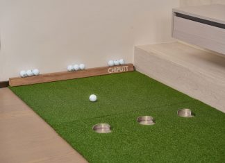 Indoor putting green with golf balls and equipment for golf practice at home.