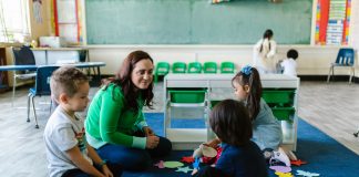 Teacher and children engaged in educational activities on a classroom floor.