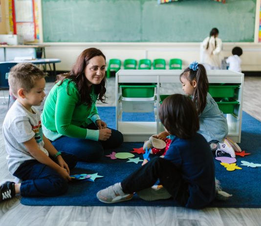 Teacher and children engaged in educational activities on a classroom floor.