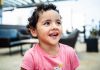 Cheerful young girl with curly hair smiling brightly in an indoor setting, exuding happiness.