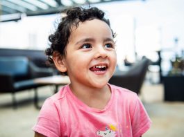 Cheerful young girl with curly hair smiling brightly in an indoor setting, exuding happiness.